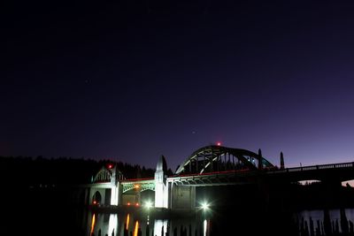 Illuminated bridge over river against sky at night