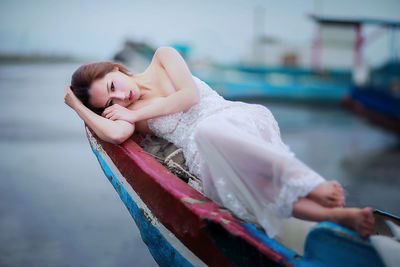 Beautiful female model in white evening gown lying on boat at sea