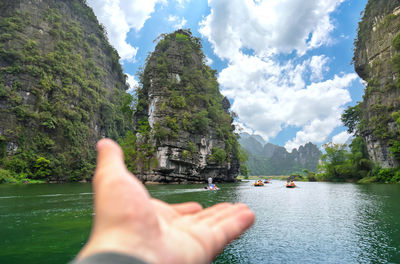 Cropped image of hand by sea against sky