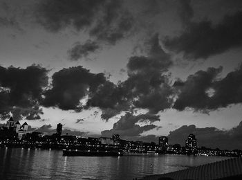 Illuminated bridge over river against cloudy sky at dusk