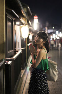 Side view portrait of woman standing on footpath at night