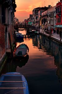 Boats moored on river in city against sky during sunset