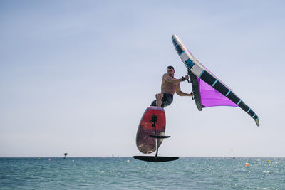 Shirtless young man with hydrofoil over sea on sunny day