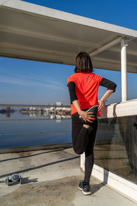 Back view of young female athlete is taking a break and doing stretching on a boat in the harbor