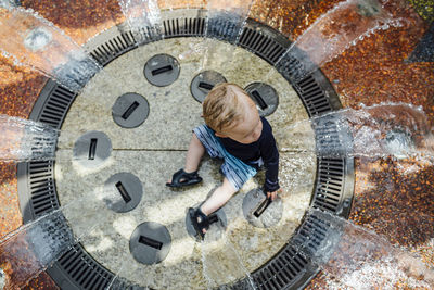 High angle view of baby boy sitting amidst fountain at water park