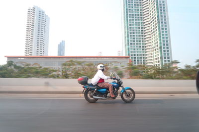Man riding motorcycle on road against buildings in city