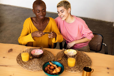 Lesbian couple photographing breakfast on table at home