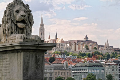 Lion statue on chain bridge against buildings in city