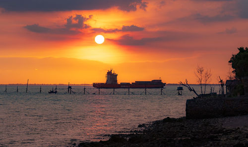 Silhouette wooden posts in sea against orange sky