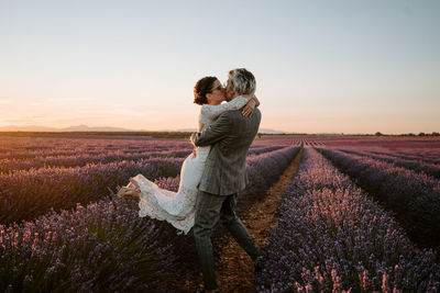 Rear view of woman with umbrella on field against sky during sunset