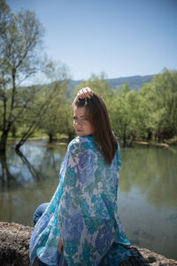 Young woman looking at lake against trees
