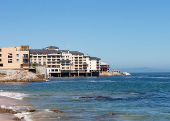 Buildings by sea against clear blue sky