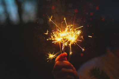 Close-up of man holding illuminated sparklers at night