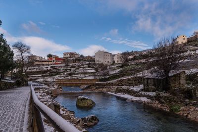 View of buildings by river against cloudy sky