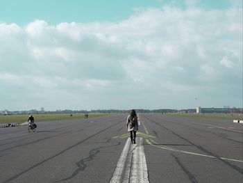 Rear view of woman walking on airport runway against sky