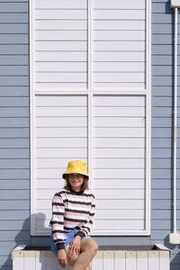 Full length of young woman wearing hat siting against wall