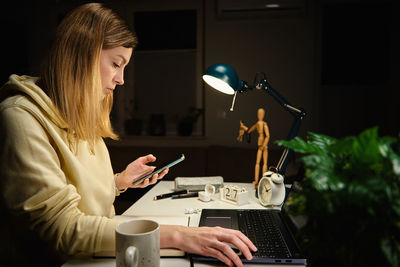 Woman works at home office at night, using laptop