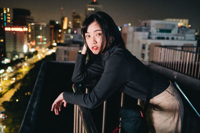 Portrait of woman standing by railing in city at night