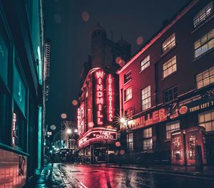 Illuminated street amidst buildings against sky at night