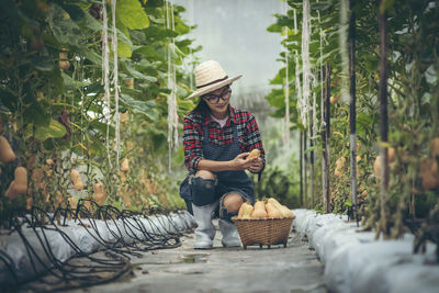 Full length of smiling man sitting by basket against plants