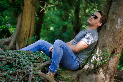 Side view of man sitting on tree trunk in forest