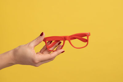 Cropped hand of woman holding red rose against yellow background