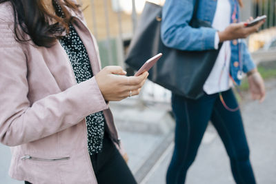 Midsection of female friends using smart phones while walking in city