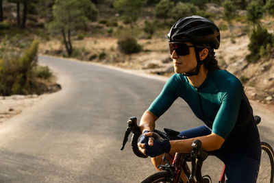Mature woman training road bike, climbing a mountain road, resting sit on the bike, side view