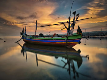 Fishing boats moored in sea against sky during sunset