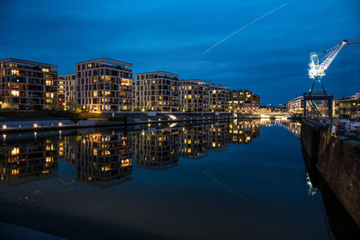 Illuminated buildings by river against sky in city at night