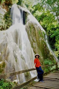 Portrait of woman standing against waterfall in forest