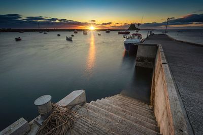 Boats moored at harbor against sky during sunset