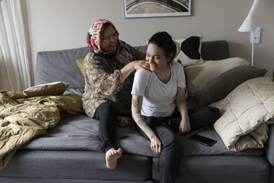 Happy woman with paraplegia being massaged by mother while sitting on sofa at home