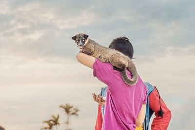 Rear view of woman with dog standing against sky