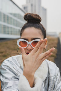 Portrait of woman in sunglasses gesturing against building