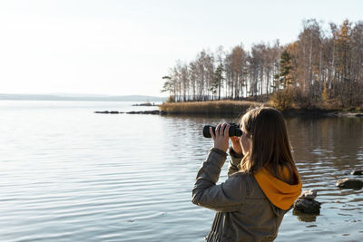 Woman looking through binoculars at birds on lake bird watching, ecology research nature, reserve