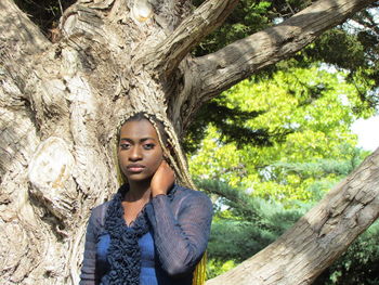 Portrait of beautiful young woman against tree trunk