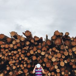Man with obscured face standing against firewood stack