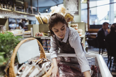 Young female owner arranging package food in display cabinet at store