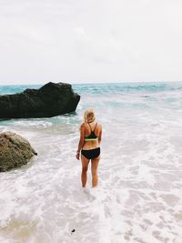 Rear view of woman standing on beach against sky