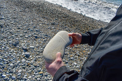 Midsection of man holding rock while standing at beach