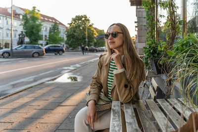 A woman sits at a wooden table in a street cafe in sunglasses