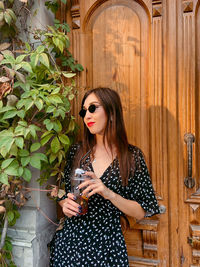 Young woman standing against door on sunny day