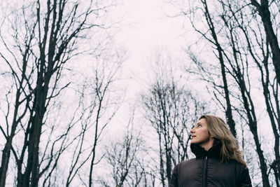 Woman standing by bare trees in winter
