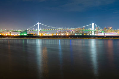 Illuminated bridge over river against sky in city at night