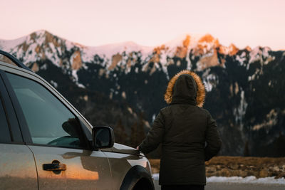 Rear view of man standing by car against mountains at sunset
