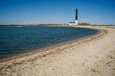 Lighthouse by sea against blue sky