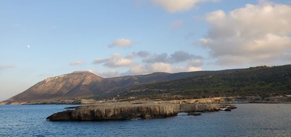 Scenic view of sea by mountain against sky