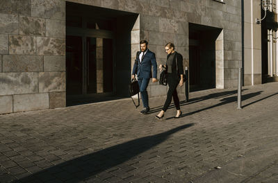 Female and male colleagues discussing while walking on footpath in city