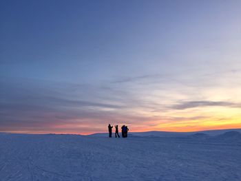 People on snowcapped landscape against sky during sunset